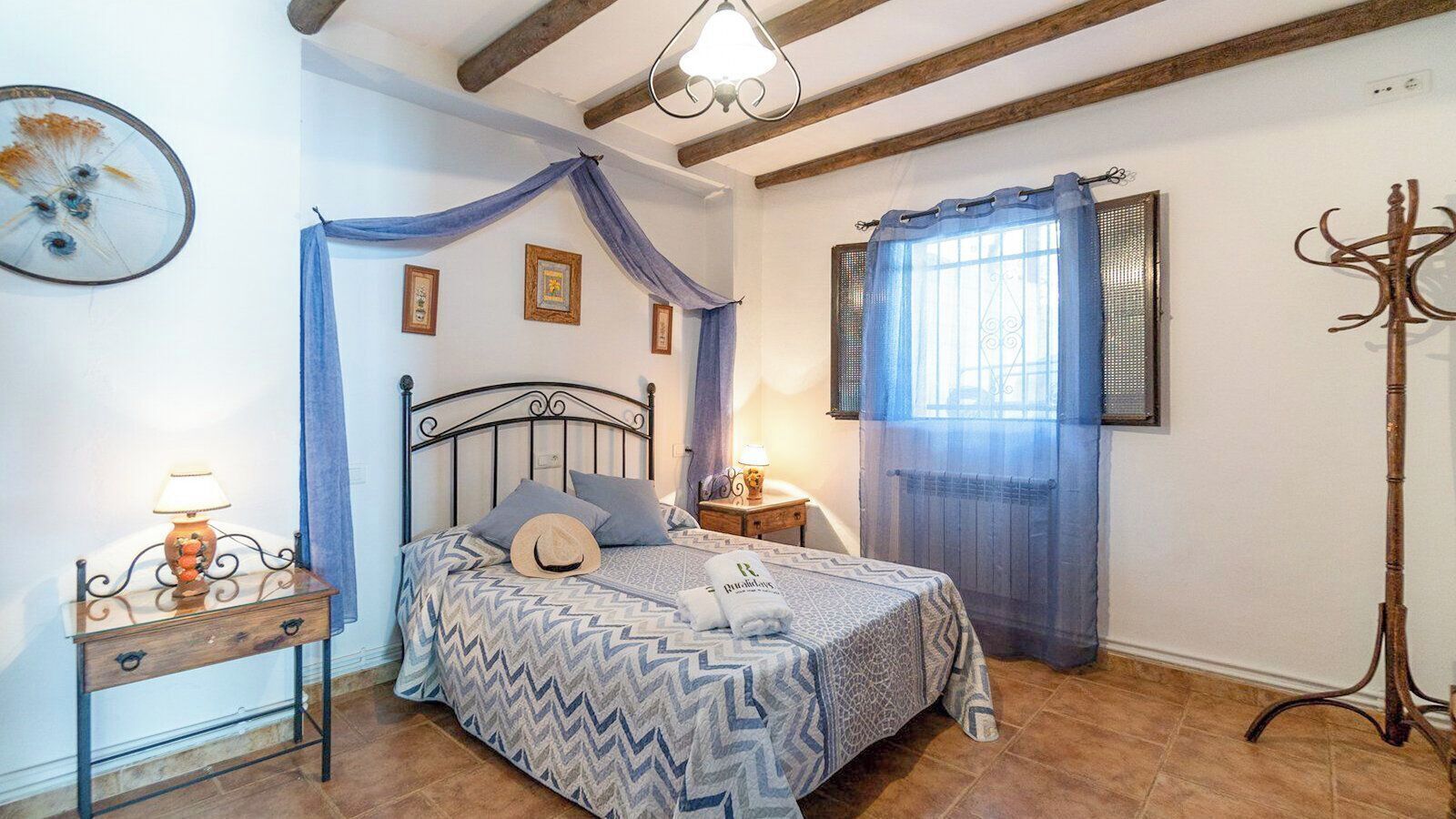 A bedroom with a bed, a bedside table with a lamp, a window with curtains, and a coat rack.