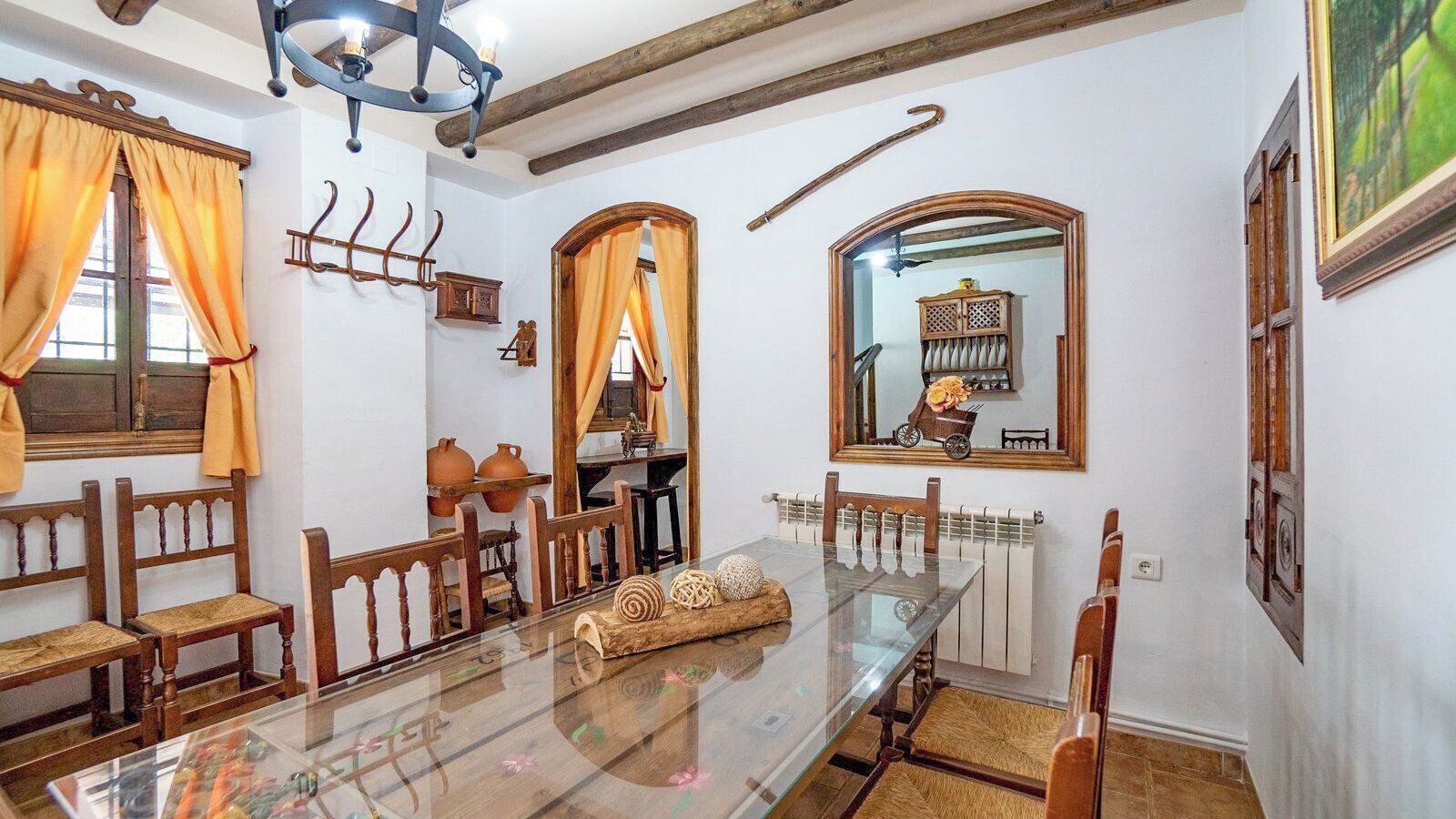 Comedor con mesa de vidrio, sillas de madera, un radiador y un espejo en la pared.