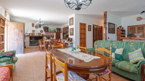 A cozy living room with a wooden dining table, green sofa, and a fireplace. - Cortijo rural Majolero Castillo de Locubín by Ruralidays (Jaén)