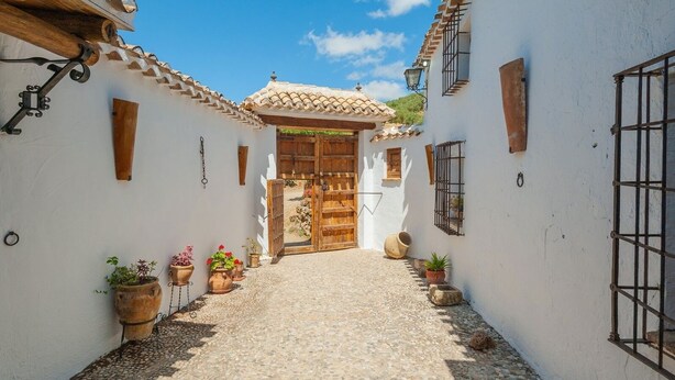 Une ruelle étroite pavée de pierres, avec des murs blancs et des portes en bois, qui mène à une cour.
