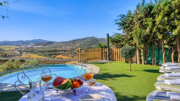 A poolside dining area with a view of the countryside, a wooden fence, and a small tree.
