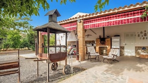 An outdoor patio with a grill, chairs, and a stone floor.