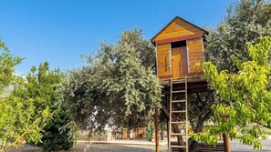 A wooden treehouse with a ladder, surrounded by trees and a clear sky.