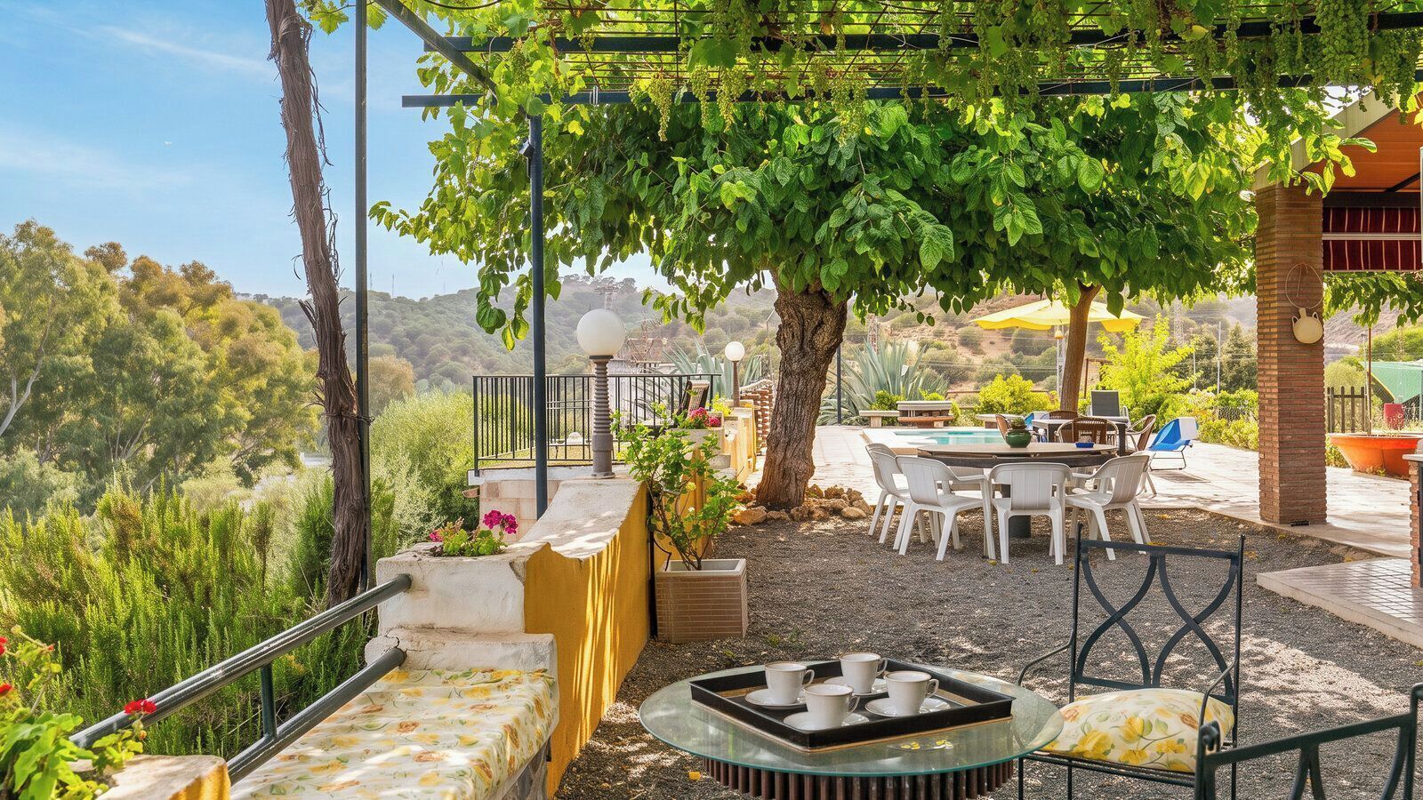 Une terrasse extérieure avec une table et des chaises, une pergola couverte de plantes grimpantes et une vue sur le paysage environnant.