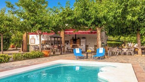 A pool area with a barbecue setup, lounge chairs, and a building with a red and white facade.