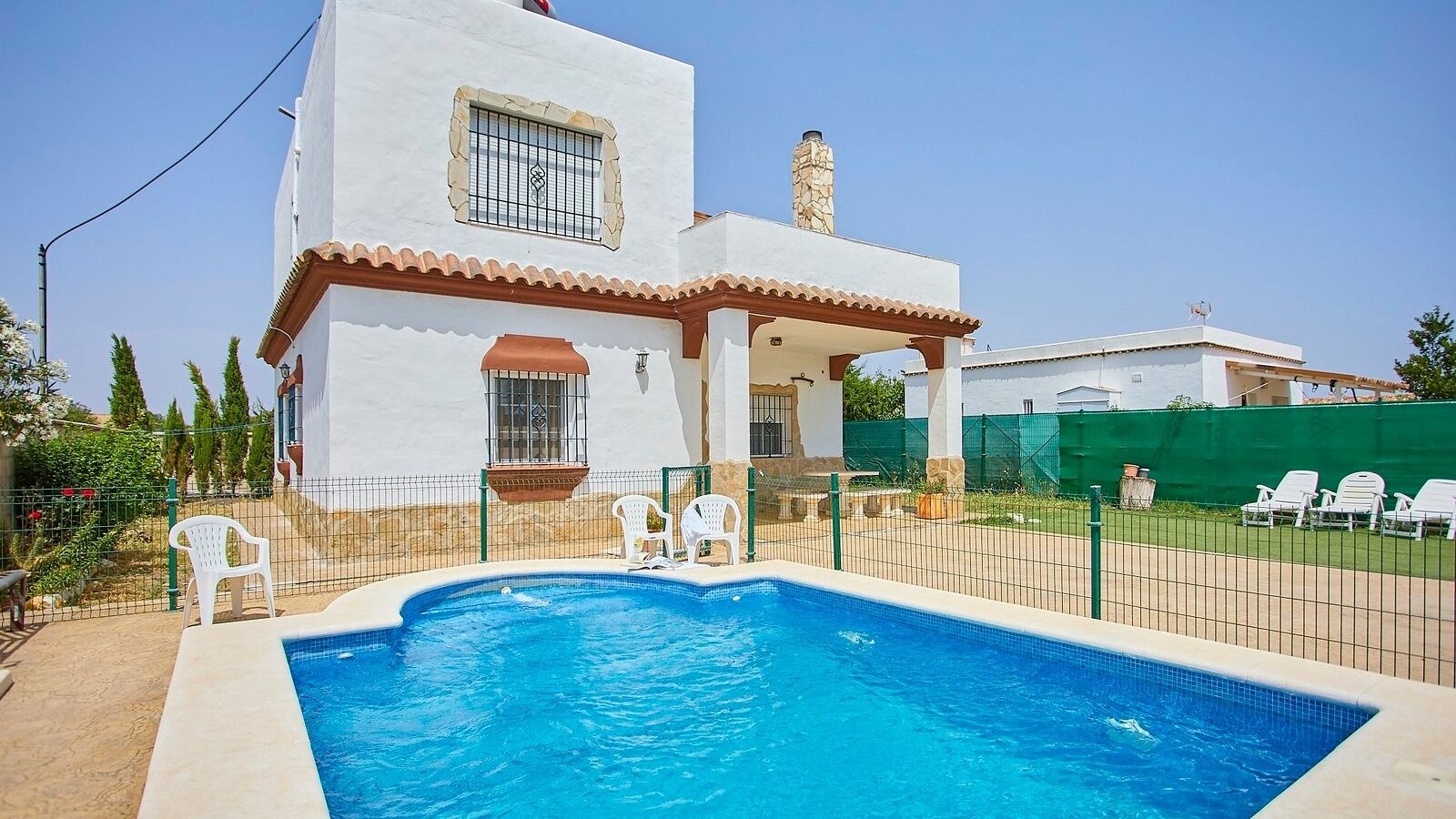 A two-story house with a swimming pool, white walls, and a green fence.