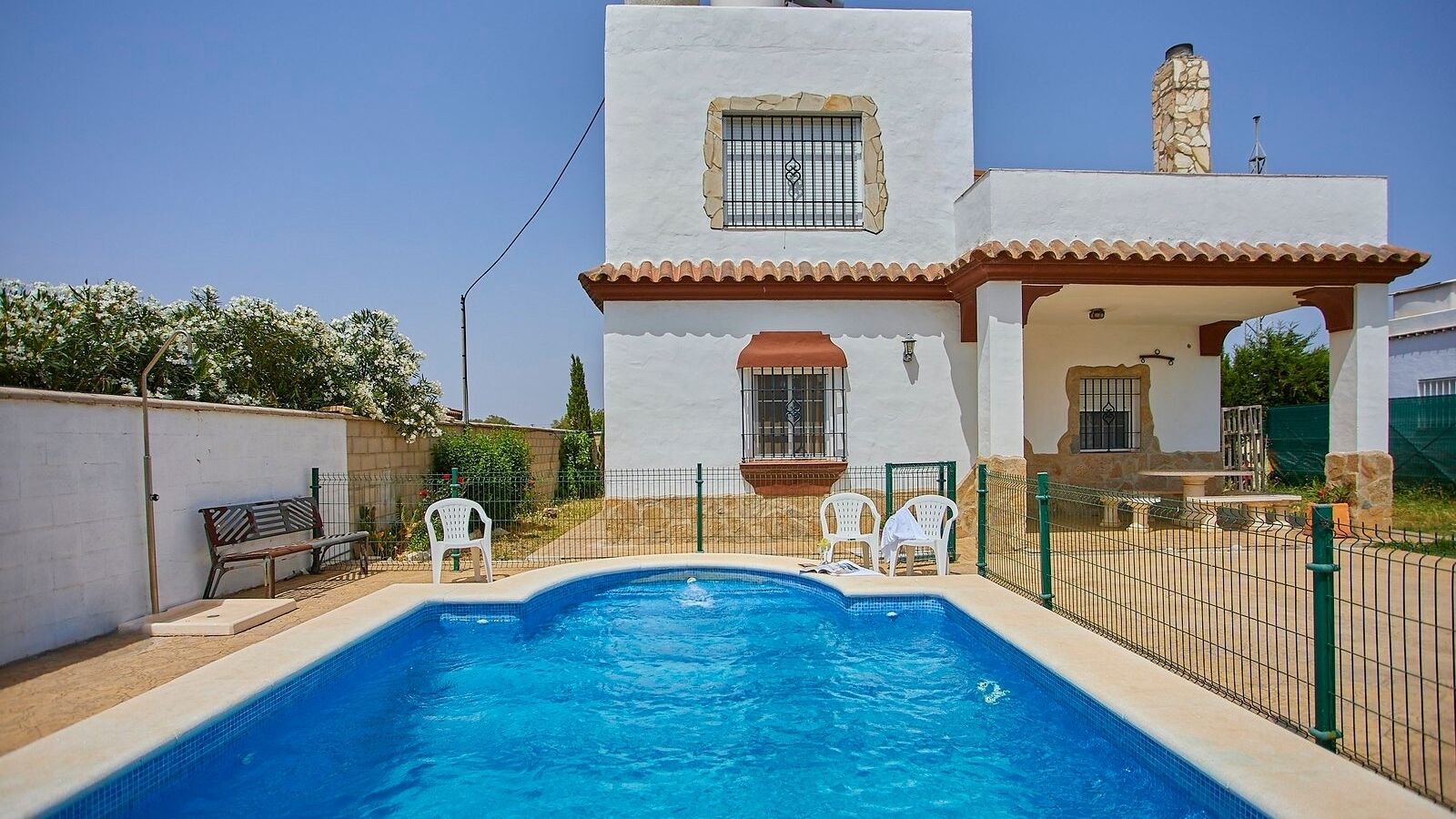Une piscine avec un bâtiment blanc en arrière-plan, un patio délimité par une clôture et un banc.