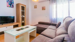 Una sala de estar moderna con un televisor de pantalla plana, una mesa de centro de cristal, un sofá gris y un mueble de madera con puertas de vidrio.