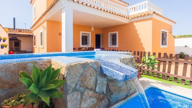 Una casa con piscina, una cascada de piedra y valla de madera.