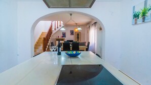 Un comedor con una mesa larga, sillas, un cuenco, copas de vino y una botella.