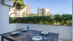 A wooden table set for four with plates, glasses, and a water bottle, overlooking a cityscape with buildings and a hedge. - Vilamoura Aldeia do Mar by Hopstays | Pool (Vilamoura)