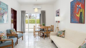A living room with a sofa, two armchairs, a dining table with chairs, and a balcony with curtains. - Vilamoura Aldeia do Mar by Hopstays | Pool (Vilamoura)