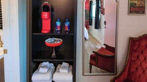 A room with a red sofa, a mirror reflecting a hallway, a shelf with towels, and a plant.