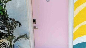 A pink door with the number 8, a potted plant, and a colorful wall mural.