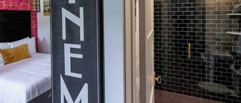 A hotel room with a bed, a bathroom with a black tiled wall, and a sign that reads 'CINEMA'.