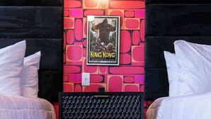 A room with two beds, a framed movie poster, a wall-mounted light, and a soundproofing panel.