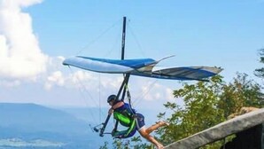 A person paragliding with a wing attached to a harness, a clear sky, and distant hills.