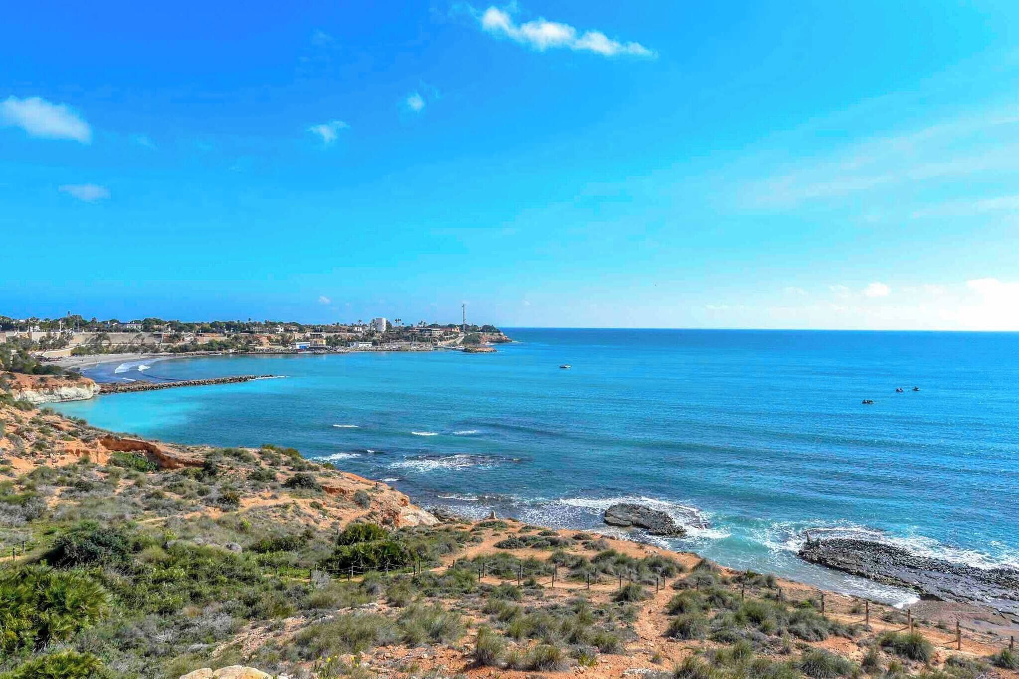 A coastal landscape with a clear view of the sea, rocky terrain, and a distant town.