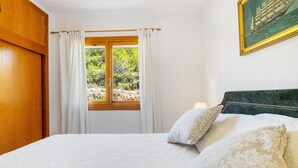 Une chambre à coucher avec un grand lit, des rideaux blancs, une porte en bois et une fenêtre donnant sur un paysage verdoyant.
