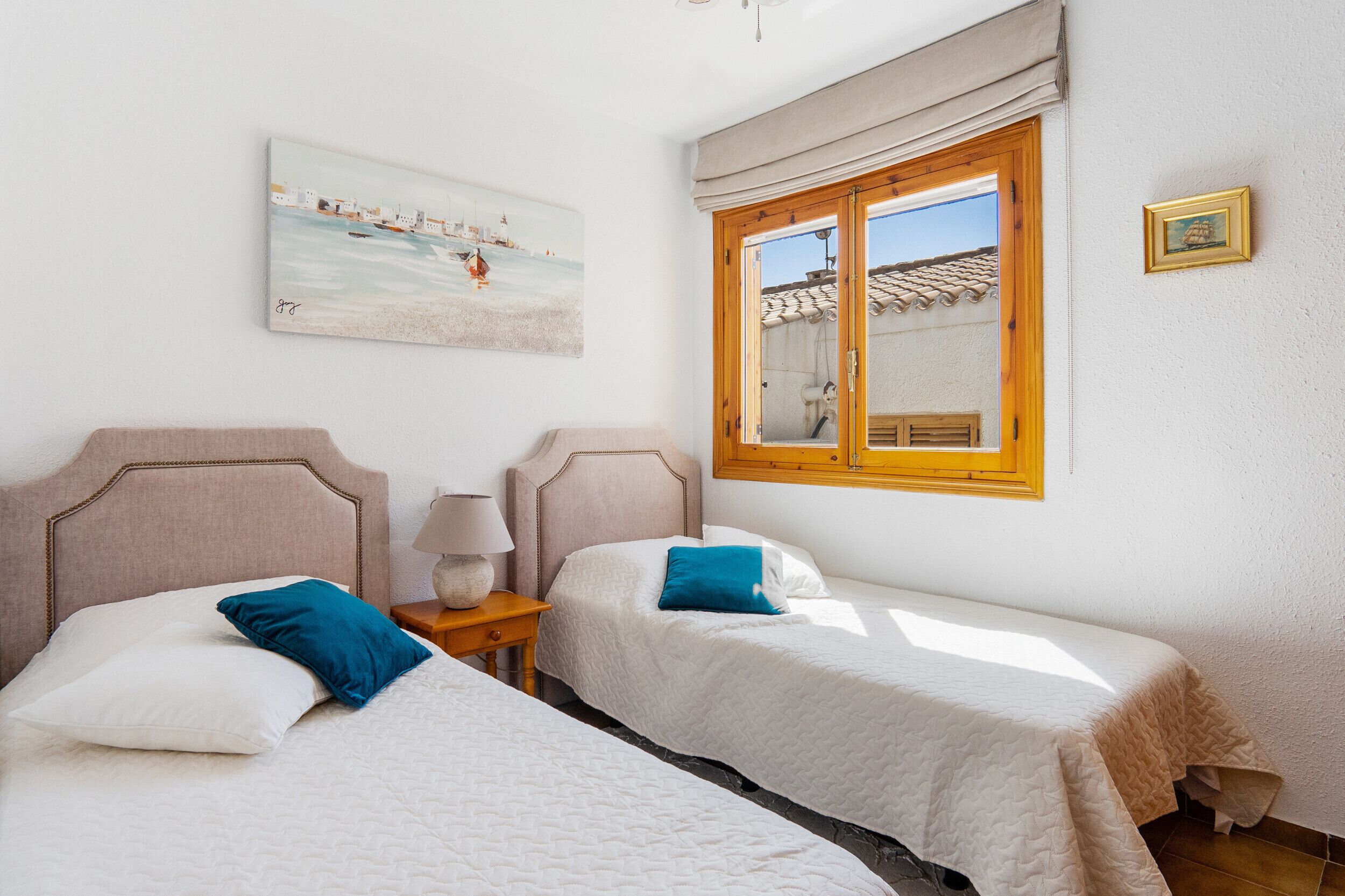 A bedroom with two beds, a painting, a window with a view of a building, and a wooden door.