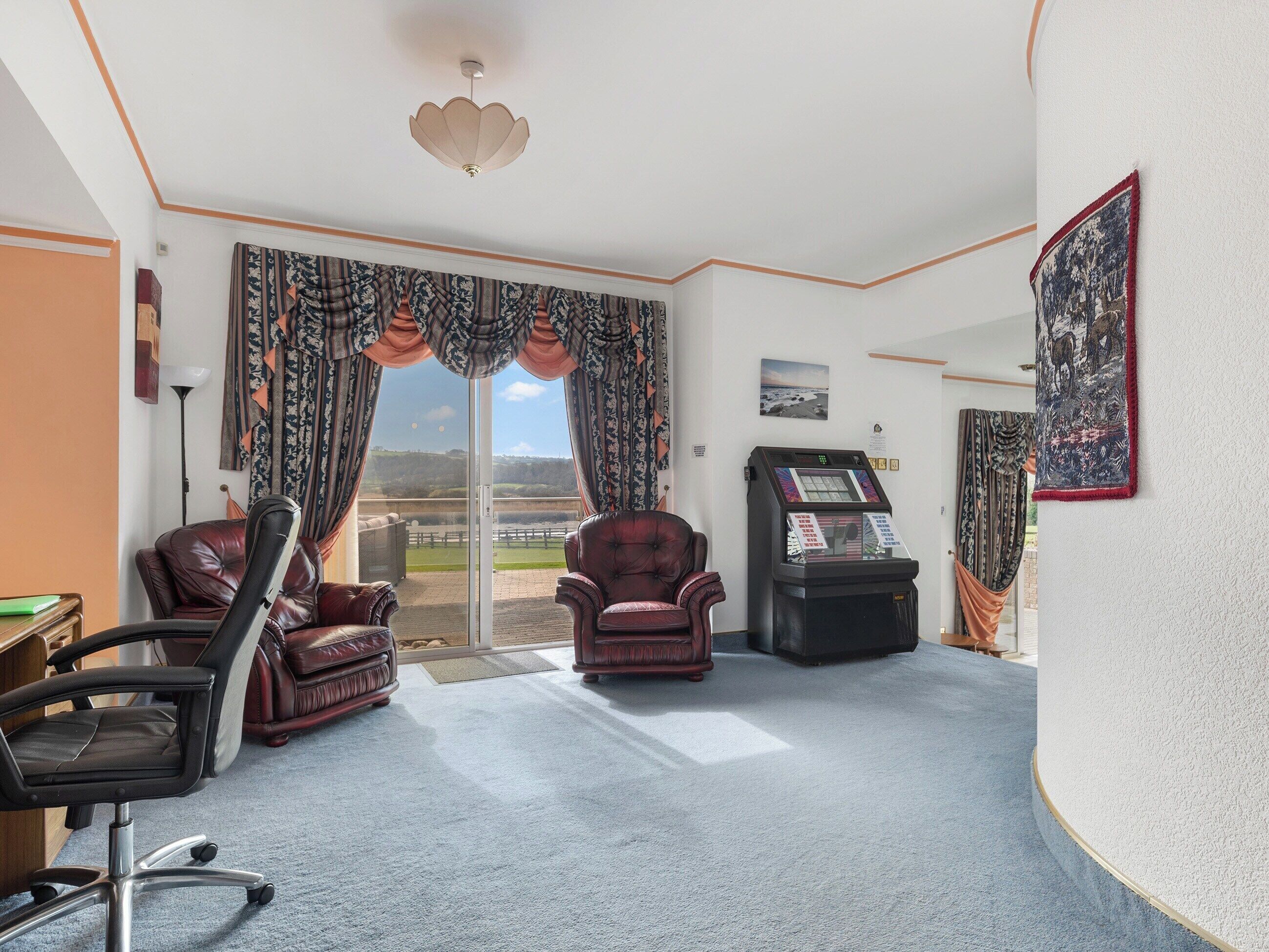 A room with two leather chairs, a desk, a slot machine, and a large window with curtains.