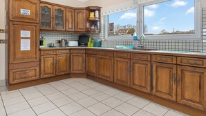 Cucina con pensili in legno, zoccolo piastrellato, finestra con vista e piano di lavoro con diversi oggetti.