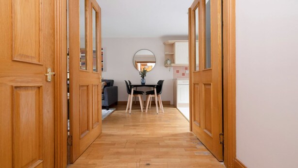 A hallway with wooden doors leading to a dining area with a table and chairs. - Bright and Cosy Flat near The Scottish Gallery (Edinburgh)