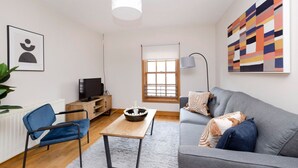 A modern living room with a grey sofa, a blue chair, a wooden coffee table, a TV, and a painting on the wall. - Bright and Cosy Flat near The Scottish Gallery (Edinburgh)