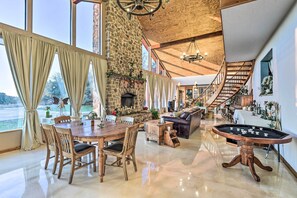 Un vaste espace de vie agrémenté d’une cheminée en pierre, d’une table à manger en bois et d’une grande fenêtre avec des rideaux.