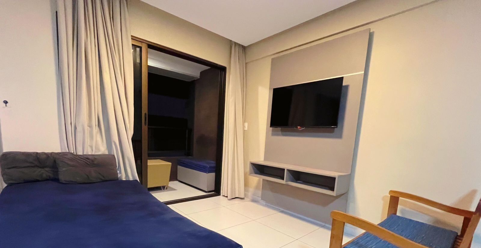 A bedroom with a bed, a TV mounted on the wall, a chair, and a small table.