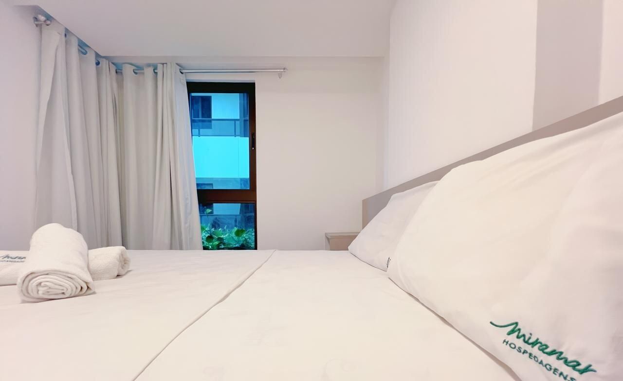 Ein Hotelzimmer mit Bett, einem fenster mit Vorhängen, Blick auf ein Gebäude und einem Handtuch auf dem Bett.