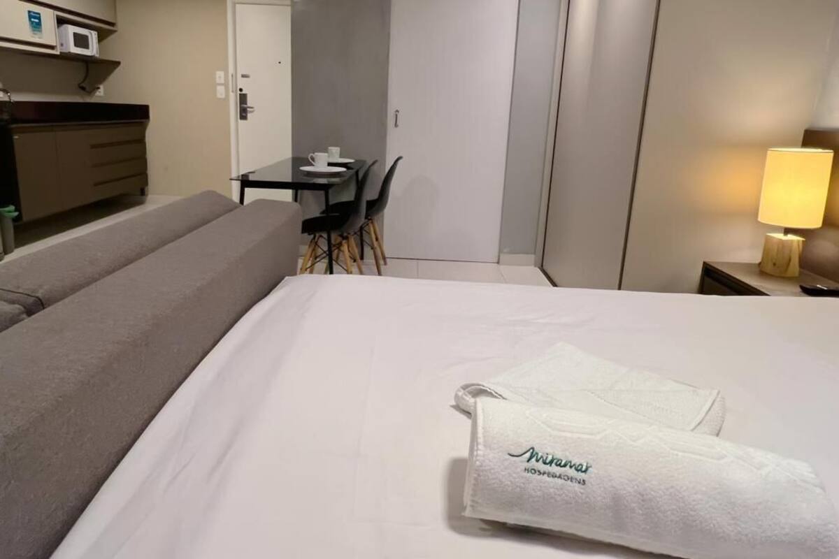 Ett hotellrum med en säng, ett skrivbord, en stol, en mikrovågsugn och ett nattduksbord med en lampa.