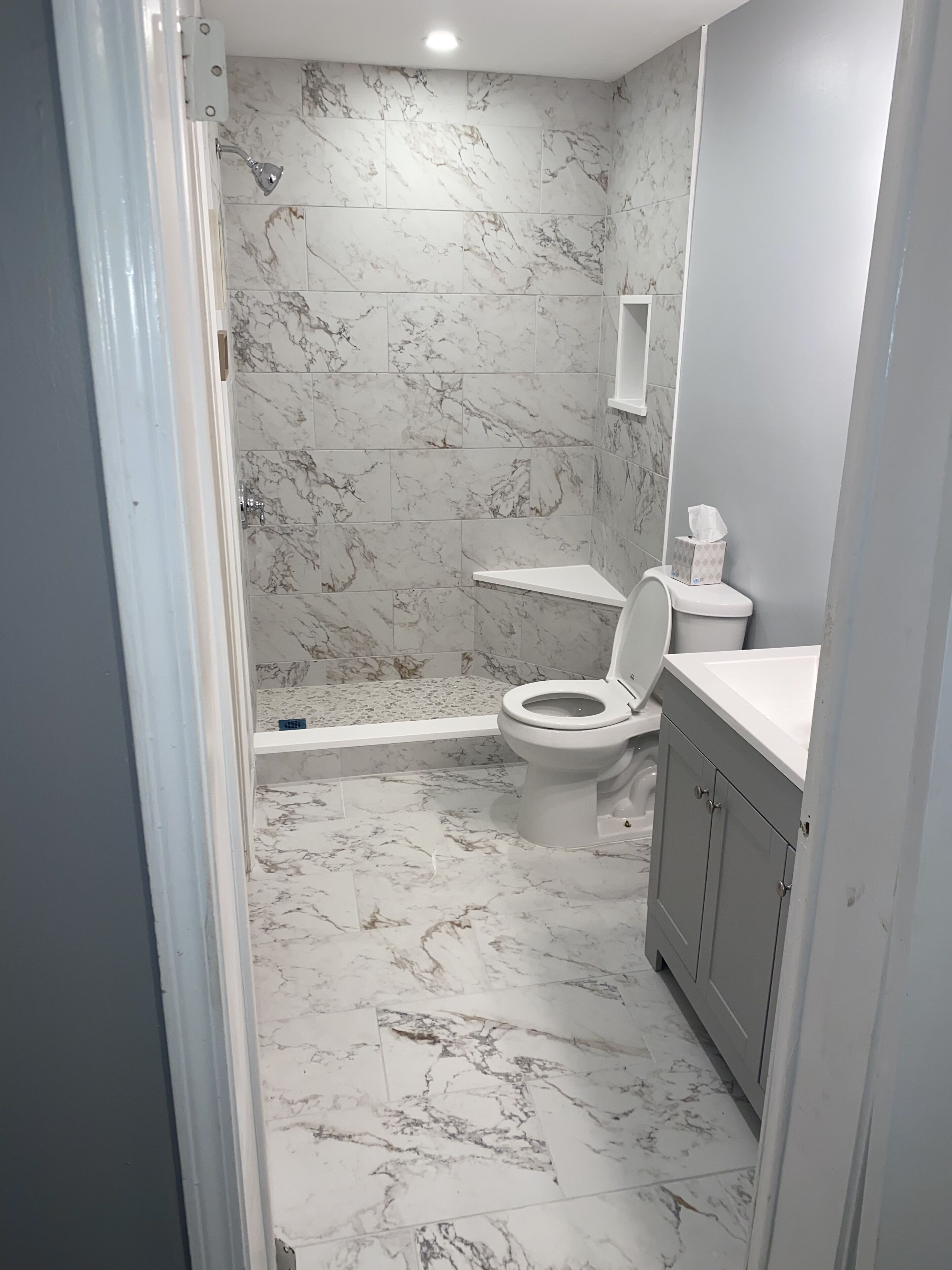 A bathroom with a shower, toilet, and marble flooring.