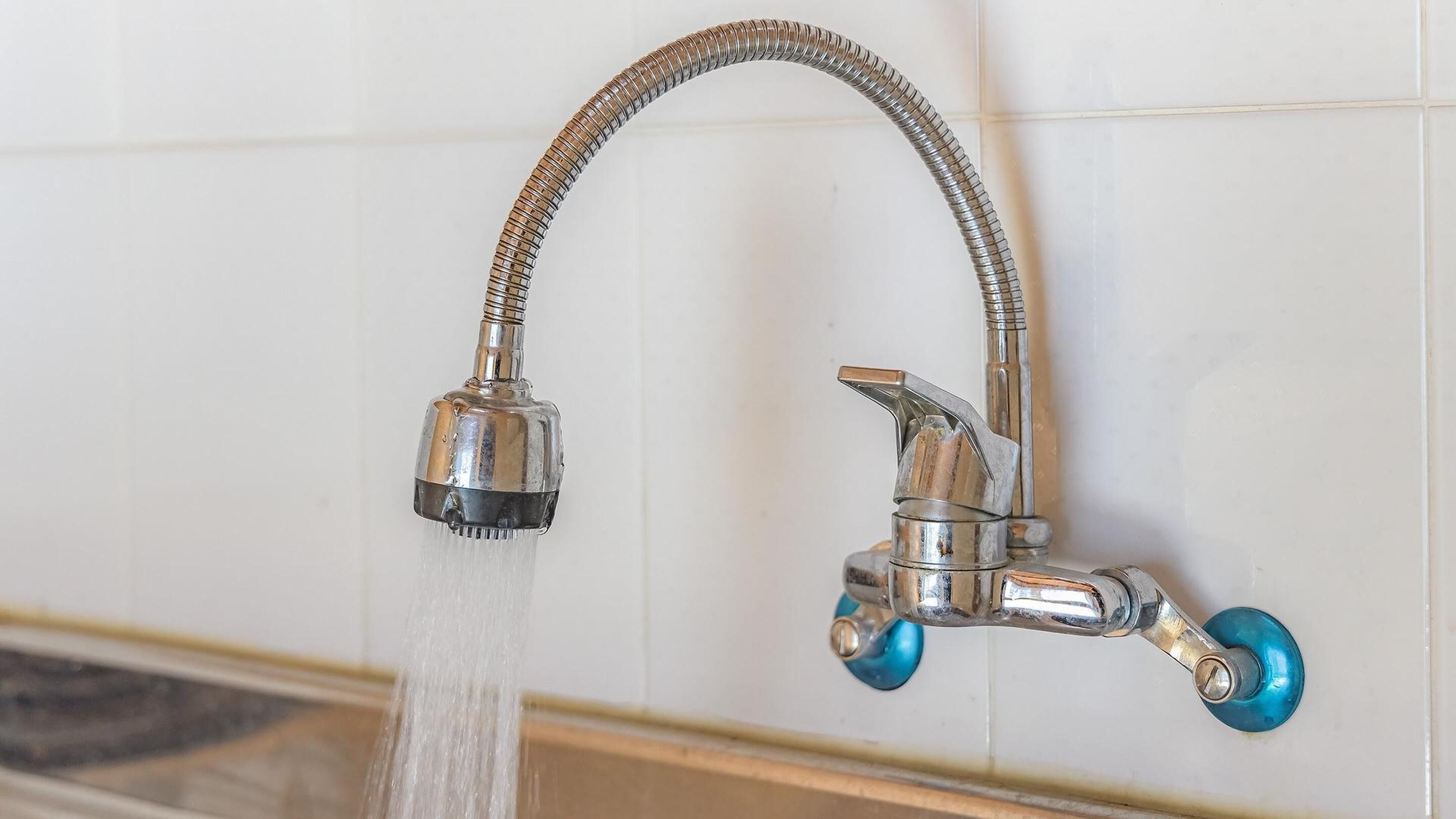 A bathroom with a chrome faucet and a flexible hose.