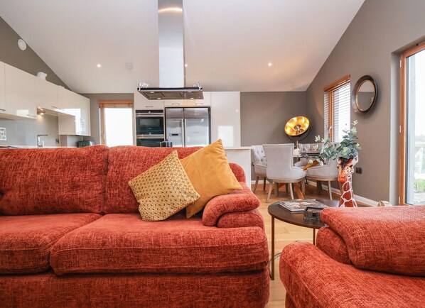 A modern living room with a red sofa, a dining area with a table and chairs, and a kitchen in the background.
