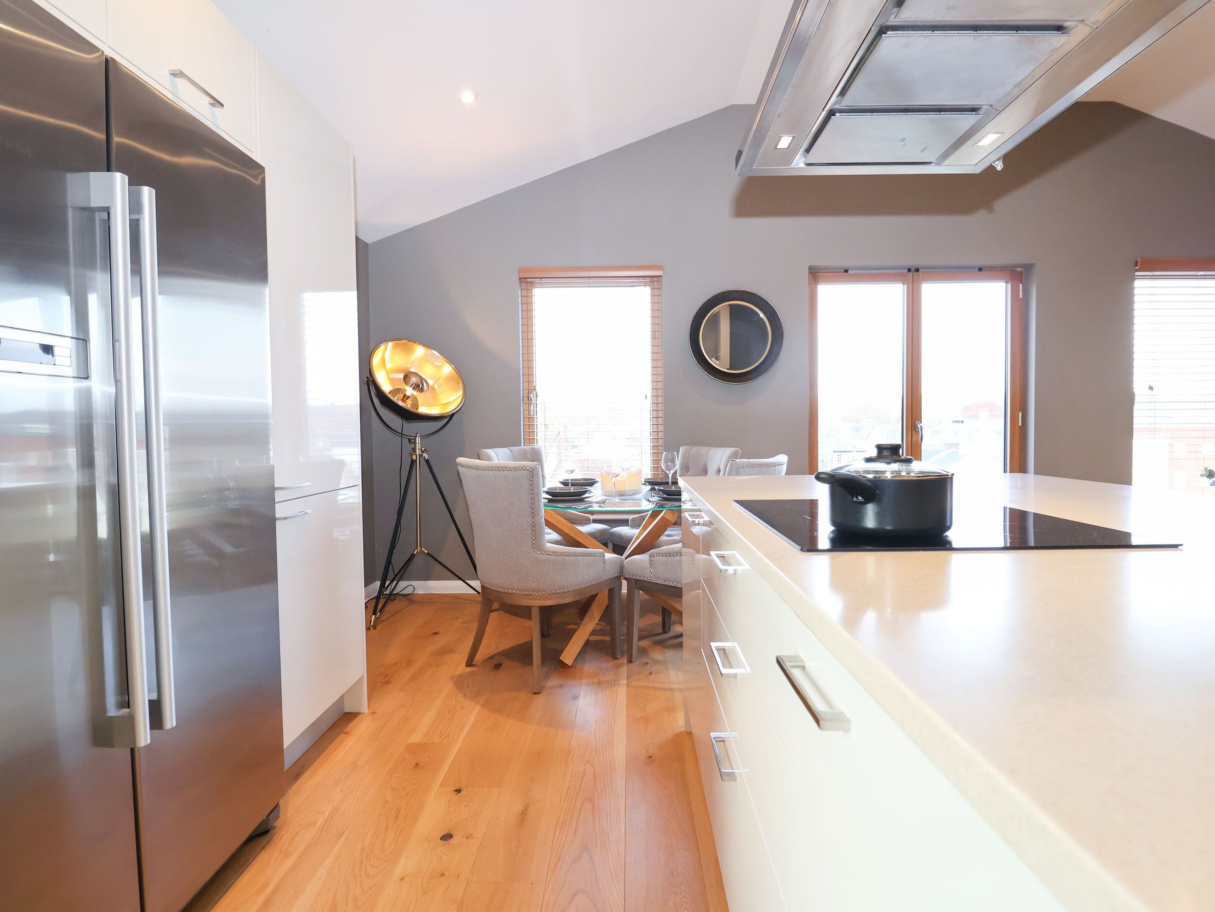A modern kitchen with a large island, stainless steel appliances, and a dining area with a chair and table.