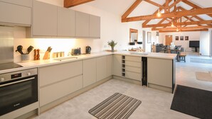 A modern kitchen with white cabinets, a Bosch oven, wooden beams, and a dining area with a TV. - The Stables (Lyme Regis)