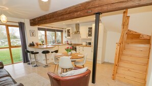 A modern kitchen with a wooden staircase, a dining area with a table and chairs, and a large window offering a view of the outdoors. - The Granary (Southam)