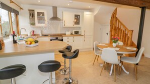 A modern kitchen with white cabinets, a wooden island with bar stools, a dining table with chairs, and a wooden staircase. - The Granary (Southam)