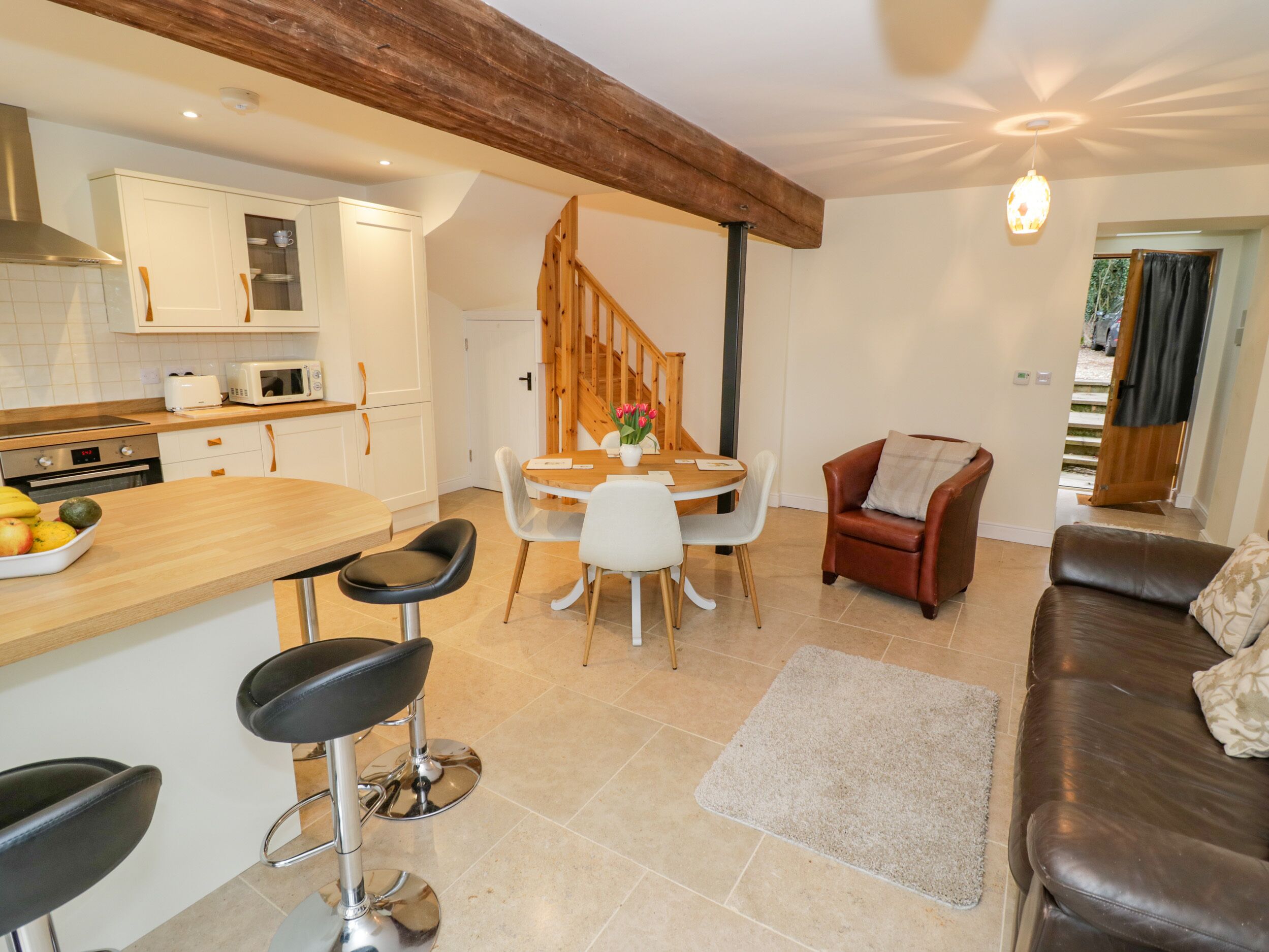 A modern kitchen with white cabinets, a wooden dining table, and a staircase leading to another level.