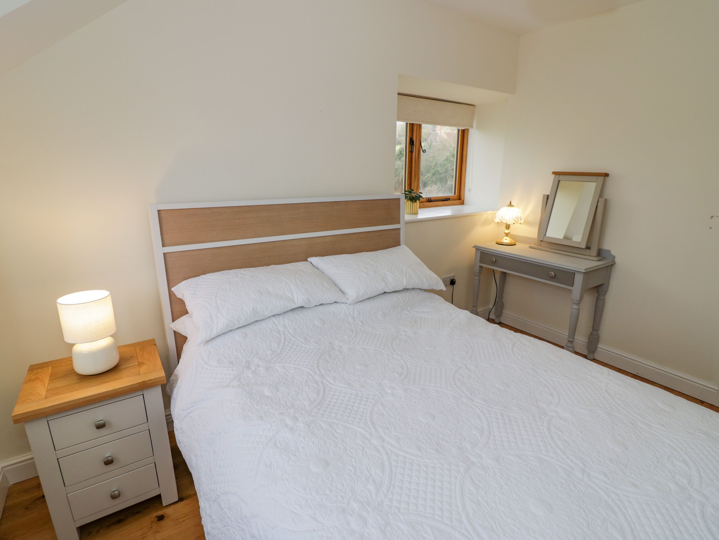 A bedroom with a bed, nightstand, dresser, and a window with a view.