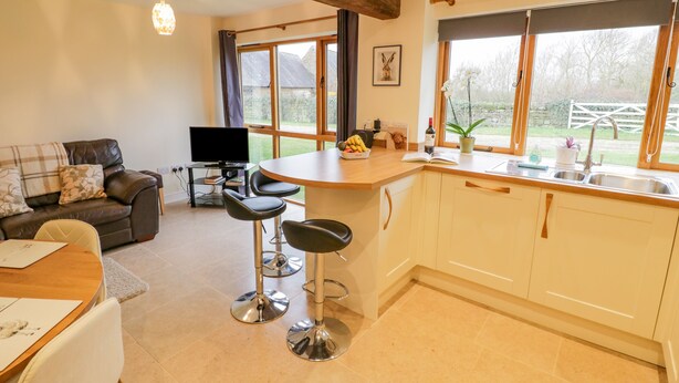 A modern kitchen with a central island, bar stools, a dining table, and a sofa. - The Granary (Southam)