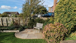 A well-maintained garden with a stone bench, a variety of flowering plants, and a brick wall. - Clover Leaf (Guisborough)