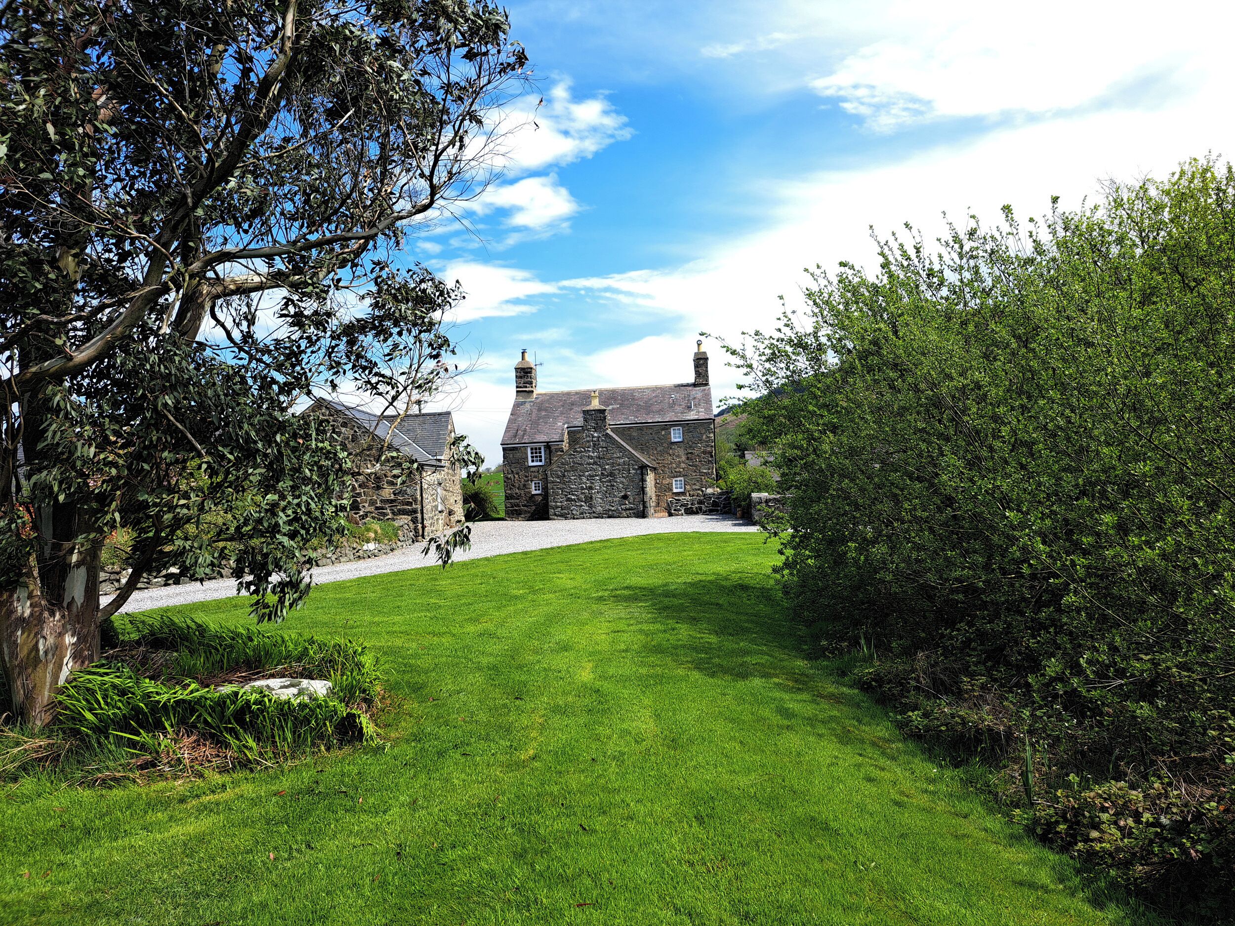 A stone house with a grassy lawn and a tree in the foreground.