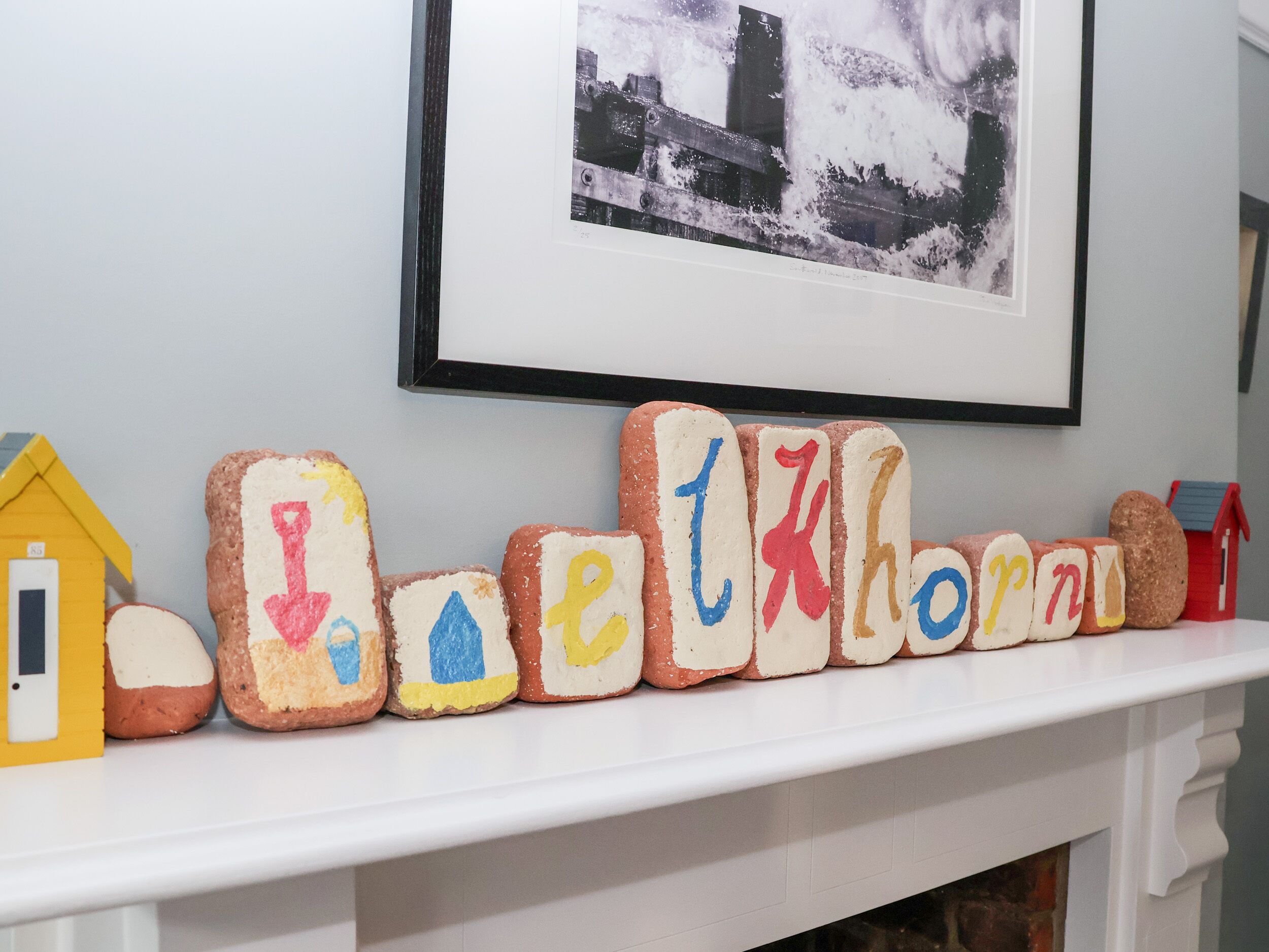 A white fireplace mantel with alphabet blocks spelling "Beckhorn" and a small yellow house model.