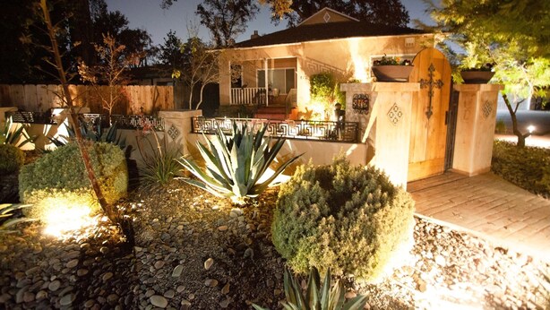 Ein Haus mit Veranda, einem verschlossenen Eingangsbereich und einem gut beleuchteten Garten mit verschiedenen Pflanzen.