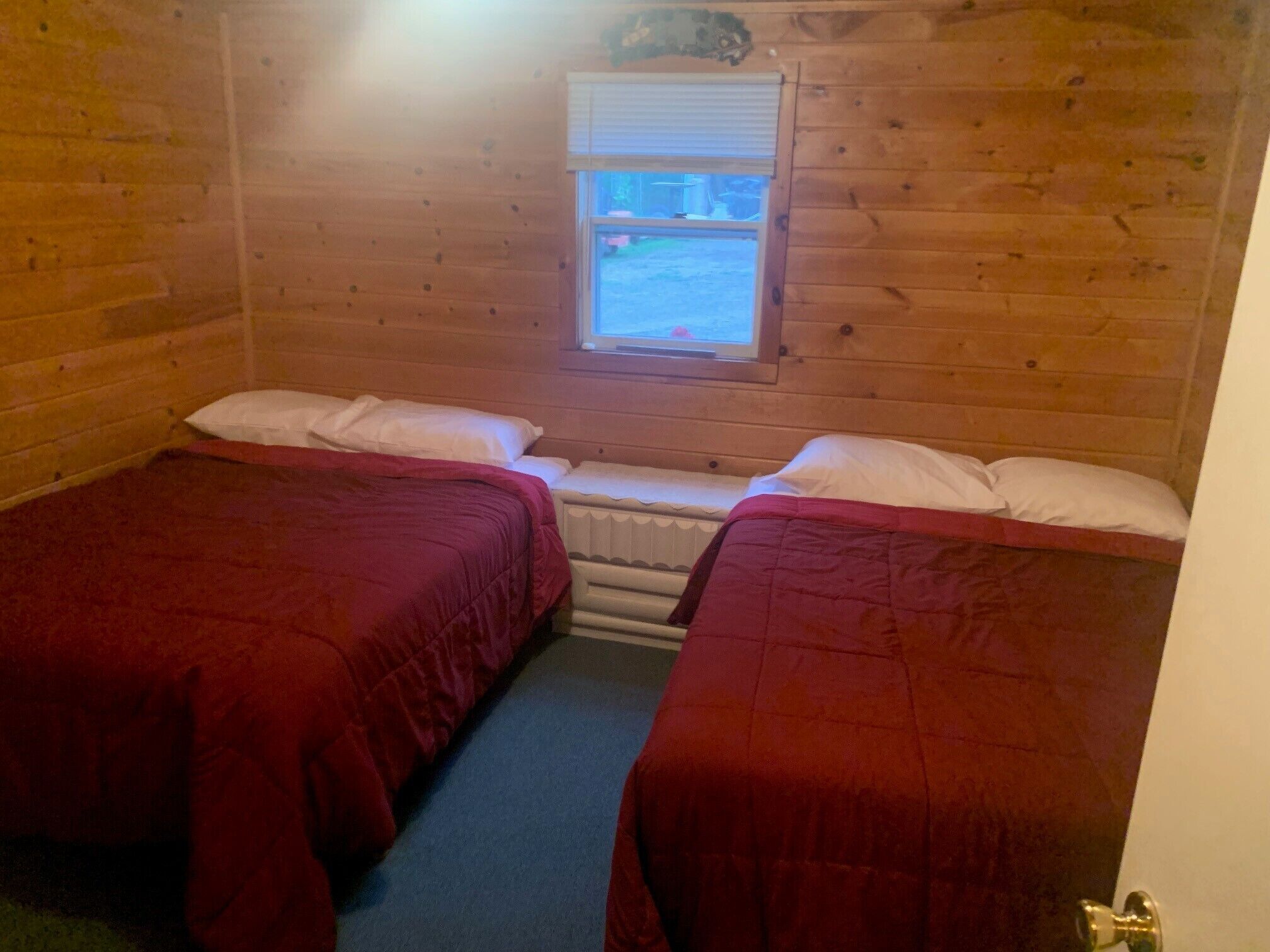 Une chambre de cabane avec deux lits, des murs en bois, une fenêtre et un radiateur.