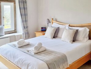 Un lit bien fait, avec du linge de lit blanc, une tête de lit en bois et une table de chevet sur laquelle se trouvent une lampe et une boîte.