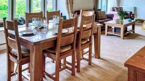 A dining area with a wooden table set for four, surrounded by chairs. There is a sofa and a small table with a vase in the background.