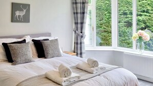 A neatly made bed with pillows, a blanket, and rolled towels.